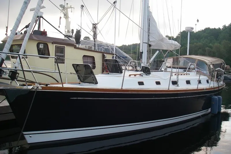 Mistral X Yacht Photos Pics 2009 Tartan 4300 sailboat docked beside a houseboat, calm waters.