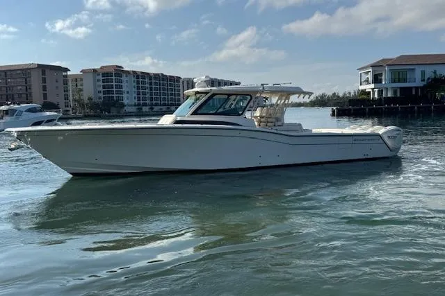  Yacht Photos Pics 2024 Grady-White Canyon 456 boat on calm water, with buildings in the background.