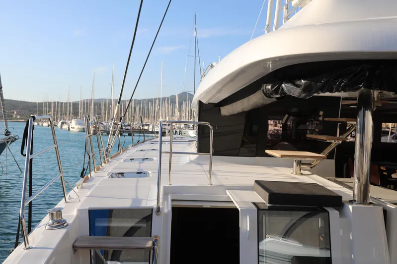  Yacht Photos Pics Lagoon 620 yacht, 2020 model, docked in a marina with clear blue water and sailboats.