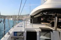 Lagoon 620 yacht, 2020 model, docked in a marina with clear blue water and sailboats.