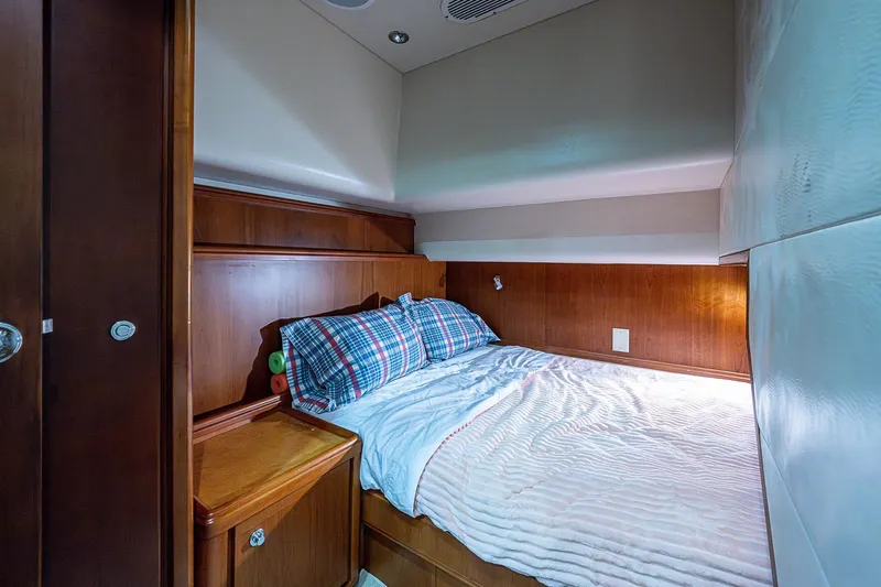  Yacht Photos Pics Cozy bedroom interior of 2006 Bertram 630 Convertible yacht with wood paneling and plaid bedding.