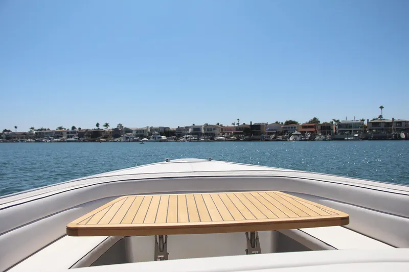  Yacht Photos Pics Bow view of 2017 Maori 50 boat with wooden table, coastal houses in background.