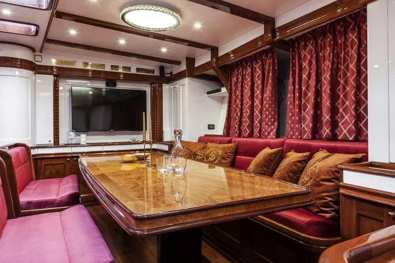 Selene Rouge Yacht Photos Pics Luxurious yacht interior with elegant wood dining table, plush red seating, and decorative curtains.