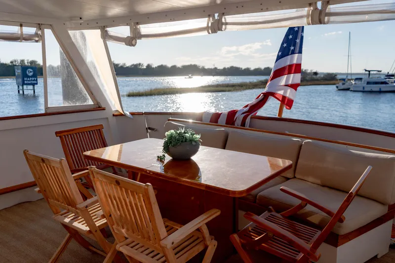 Sea Suite Yacht Photos Pics Luxurious 1974 Burger 67 yacht deck with wooden furniture and American flag, overlooking serene waters.