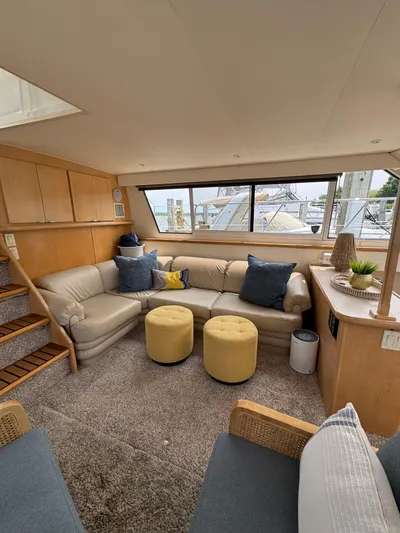 Y Knot Yacht Photos Pics 1997 Carver 405 Aft Cabin interior with beige sofa, yellow ottomans, and large windows.