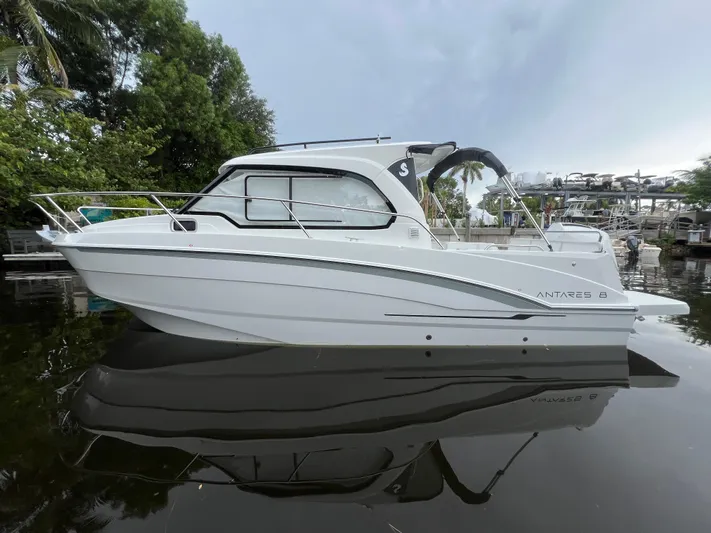  Yacht Photos Pics 2025 Beneteau Antares 8 boat on calm water, surrounded by lush greenery.