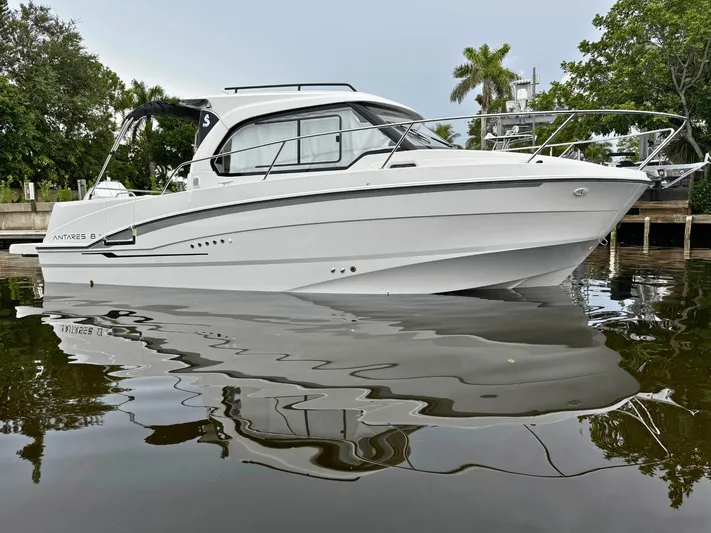  Yacht Photos Pics 2025 Beneteau Antares 8 boat on calm water, surrounded by lush greenery.