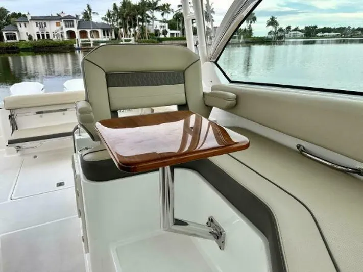  Yacht Photos Pics 2019 Pursuit DC 325 Dual Console interior with elegant seating and wooden table by a serene waterfront.