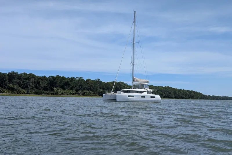 Exodus Yacht Photos Pics 2022 Lagoon 46 catamaran sailing on calm waters near a forested shoreline.