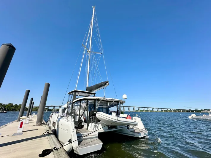 Never Say Never Yacht Photos Pics 2017 Lagoon 42 catamaran docked by a scenic waterfront under clear blue skies.