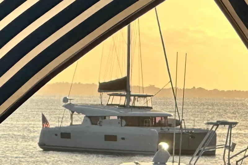 Never Say Never Yacht Photos Pics 2017 Lagoon 42 catamaran sailing at sunset, framed by striped canopy.