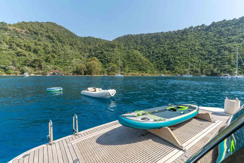  Yacht Photos Pics Luxury yacht deck with paddleboard, serene blue water, and lush green hills in the background.