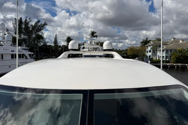  Yacht Photos Pics 2004 Mangusta 72 yacht docked under cloudy sky, surrounded by trees and waterfront homes.