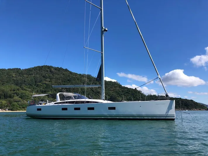  Yacht Photos Pics 2021 Jeanneau 64 yacht anchored near lush green island under clear blue sky.