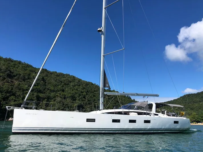  Yacht Photos Pics 2021 Jeanneau 64 yacht sailing near lush green hills under a clear blue sky.