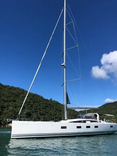  Yacht Photos Pics 2021 Jeanneau 64 yacht sailing on calm waters with lush green hills in the background.