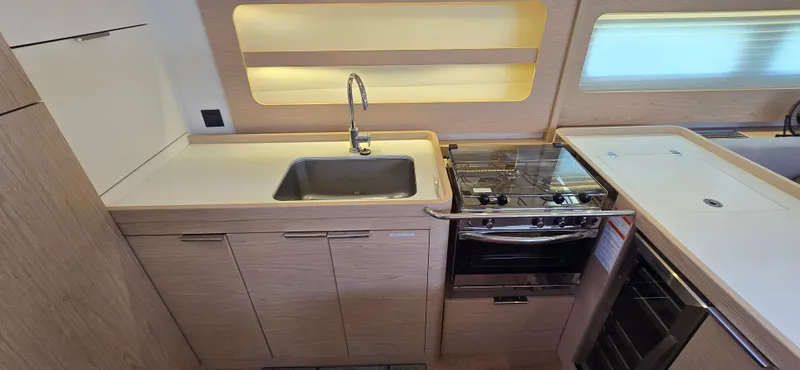 Wildflower Yacht Photos Pics Modern kitchen in 2021 Beneteau Oceanis Yacht 54 with sink, stove, and wooden cabinetry.