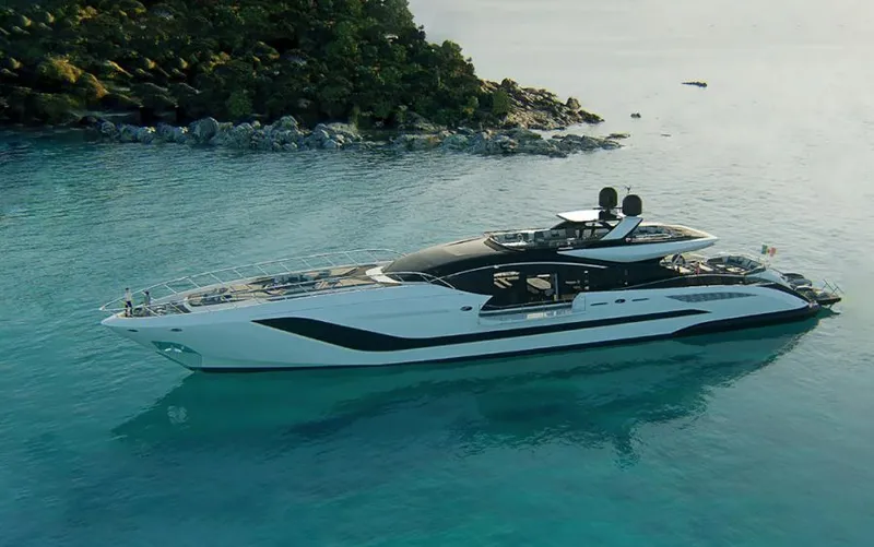 Yacht Photos Pics Luxurious 2022 Mangusta 165 REV yacht cruising in clear blue waters near a rocky shoreline.