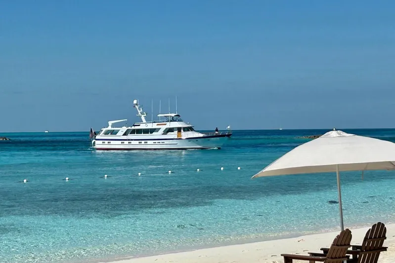 Capricho Yacht Photos Pics 1987 Burger Motoryacht cruising in clear blue waters near a sandy beach with umbrella.