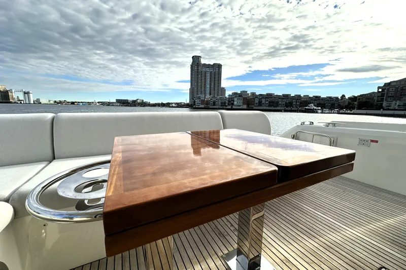 Highland Patriot Yacht Photos Pics Luxurious 2023 Prestige 590 yacht deck with wooden table, overlooking waterfront cityscape.