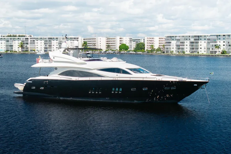 Sukha Yacht Photos Pics Luxury 2008 Sunseeker 90 Yacht cruising on a serene waterfront with modern buildings.