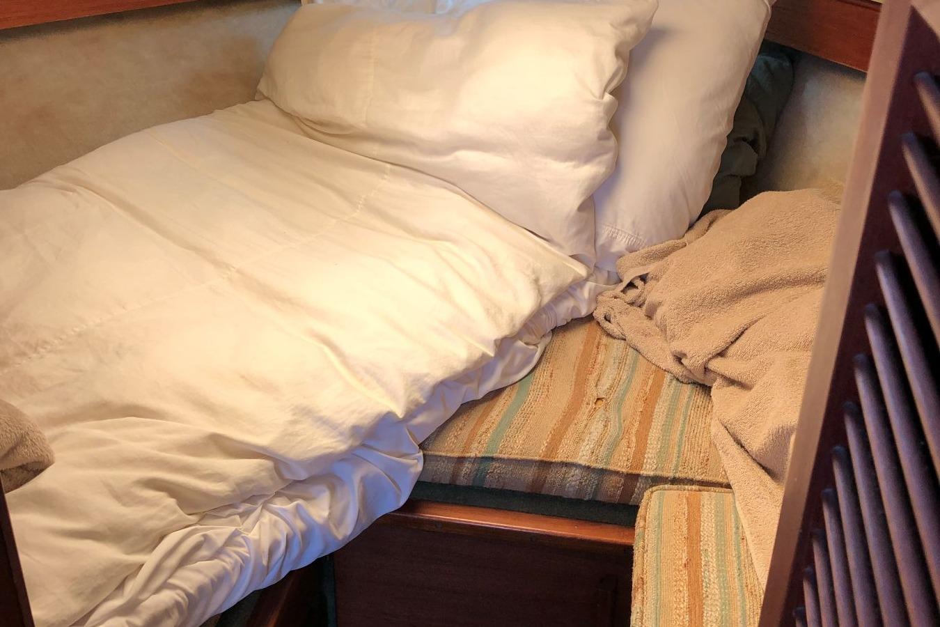 Cozy cabin bed inside 1988 Commander 30 Command Bridge boat, with white bedding and striped cushions.