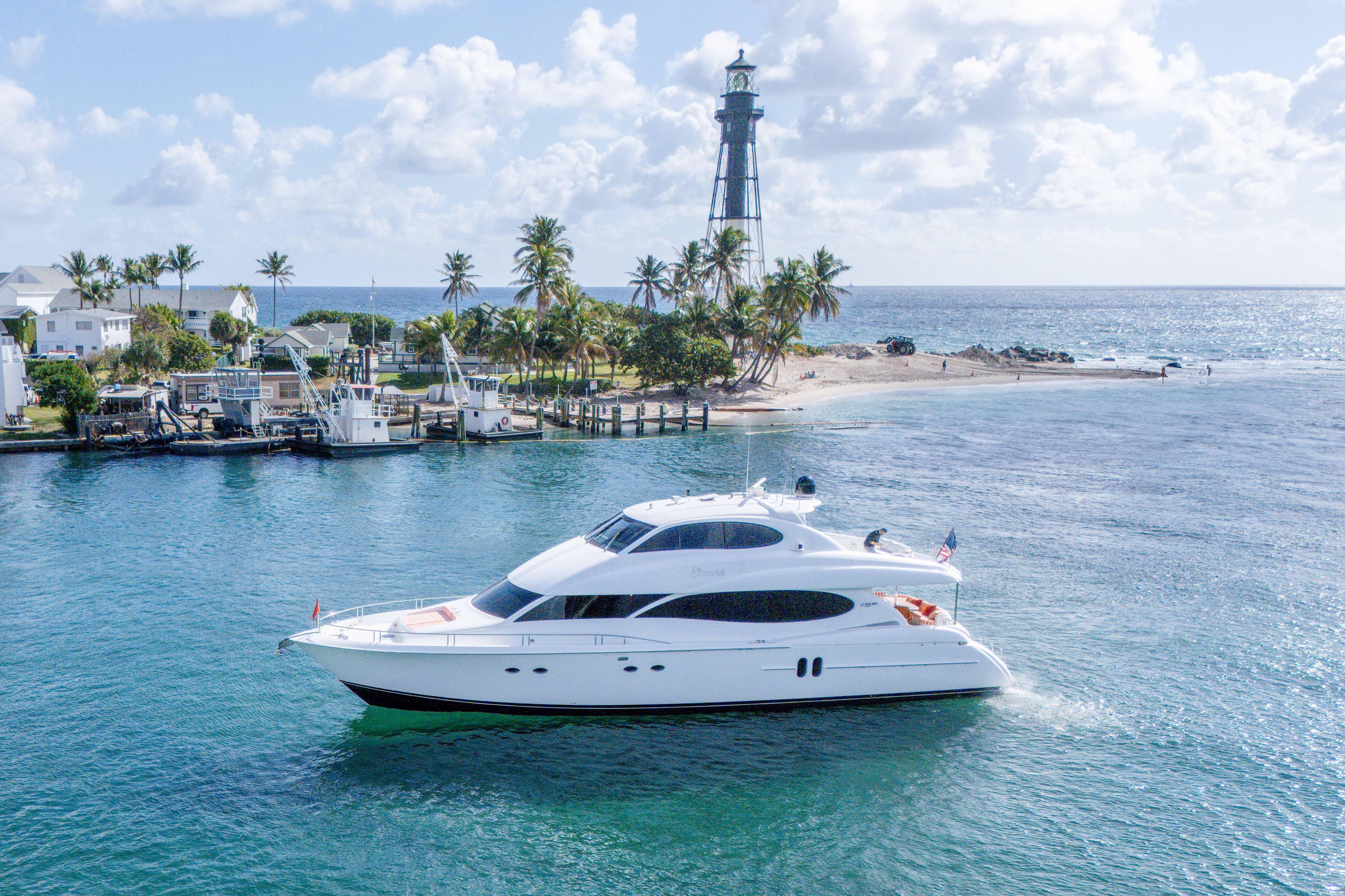 Luxury 2004 Lazzara 80 SL yacht cruising near a scenic lighthouse and palm-lined shore.