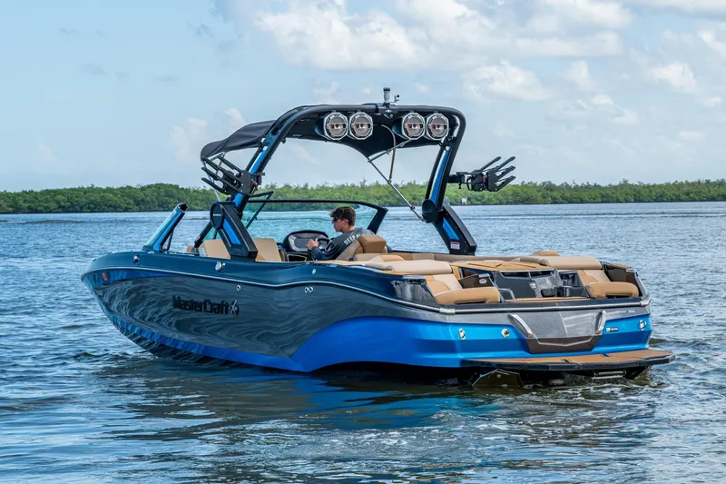  Yacht Photos Pics 2022 MasterCraft X26 boat cruising on a lake with a clear sky backdrop.