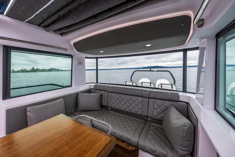 Aqvavit Yacht Photos Pics Interior of 2021 Axopar 37xc Wetbar with gray seating and wooden table, overlooking water.
