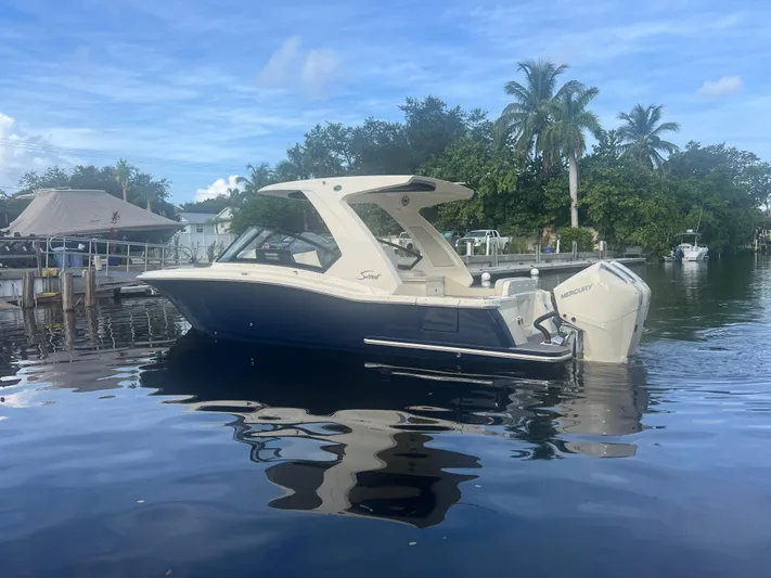  Yacht Photos Pics 2025 Scout 277 Dorado boat on calm water with lush greenery background.