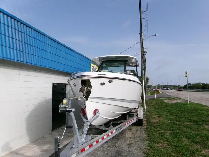  Yacht Photos Pics 2025 Monterey Elite 27 OB boat on trailer near blue-roofed building.