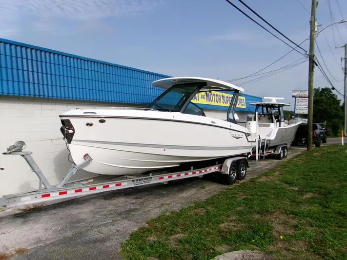  Yacht Photos Pics 2025 Monterey Elite 27 OB boat on trailer, parked outdoors near a blue-roofed building.