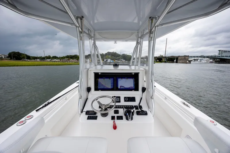  Yacht Photos Pics 2023 Contender 32 ST boat cockpit with navigation screens and steering wheel on a calm waterway.