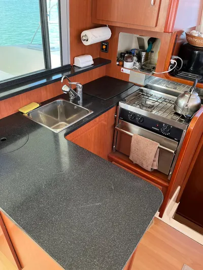Ikati Yacht Photos Pics Compact kitchen in a 2011 Leopard 39 yacht with stove, sink, and wooden cabinetry.