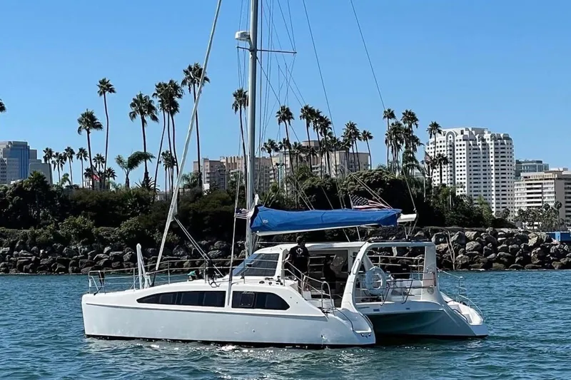 Making Waves Yacht Photos Pics 2006 Seawind 1160 catamaran sailing near a city skyline with palm trees.