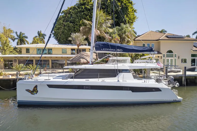  Yacht Photos Pics 2021 Leopard 50 catamaran docked by waterfront homes, featuring a butterfly decal.