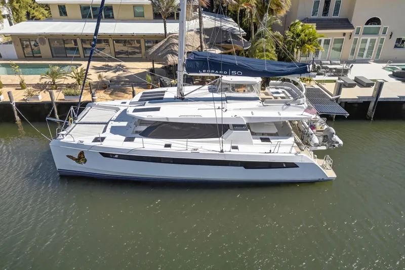  Yacht Photos Pics 2021 Leopard 50 catamaran docked by waterfront home, featuring sleek design and butterfly decal.