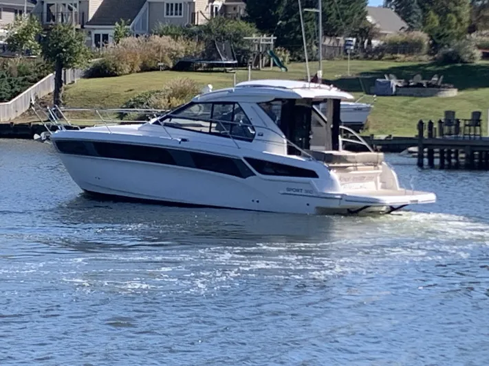  Yacht Photos Pics 2015 Bavaria S36 Coupe cruising on a serene waterway near residential area.