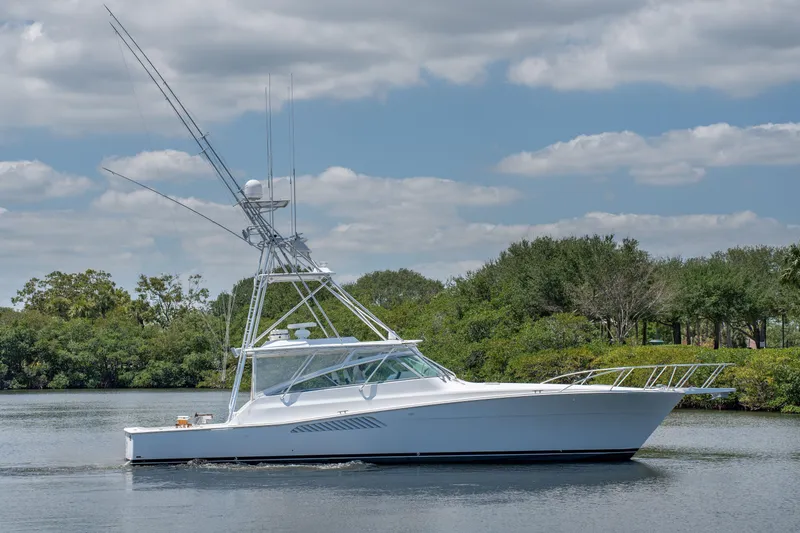 All Keyed Up Yacht Photos Pics 2001 Viking 50 Express yacht on calm water, surrounded by lush greenery and a cloudy sky.