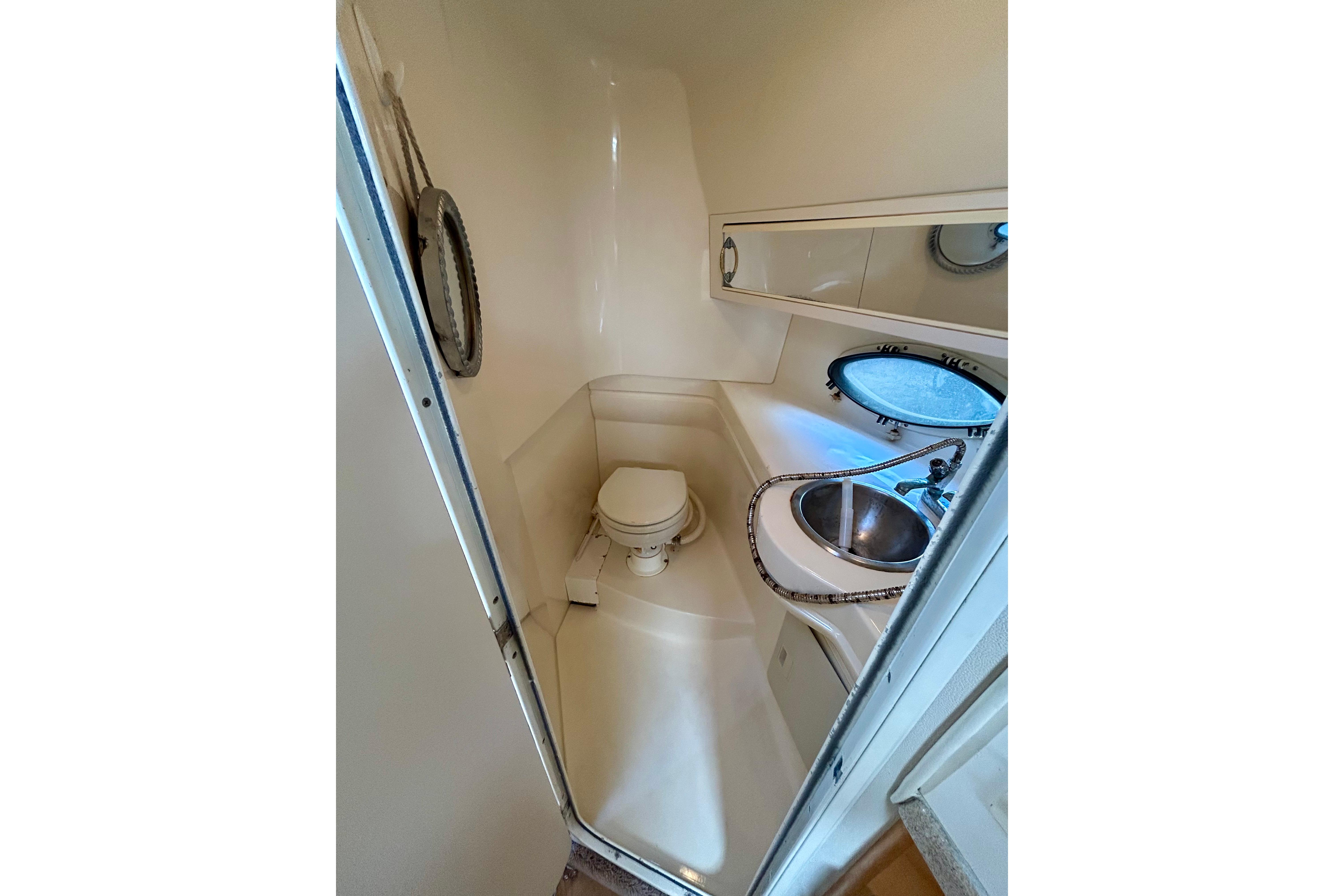 Compact bathroom in 2000 Larson 290 Cabrio boat with sink, toilet, and porthole window.