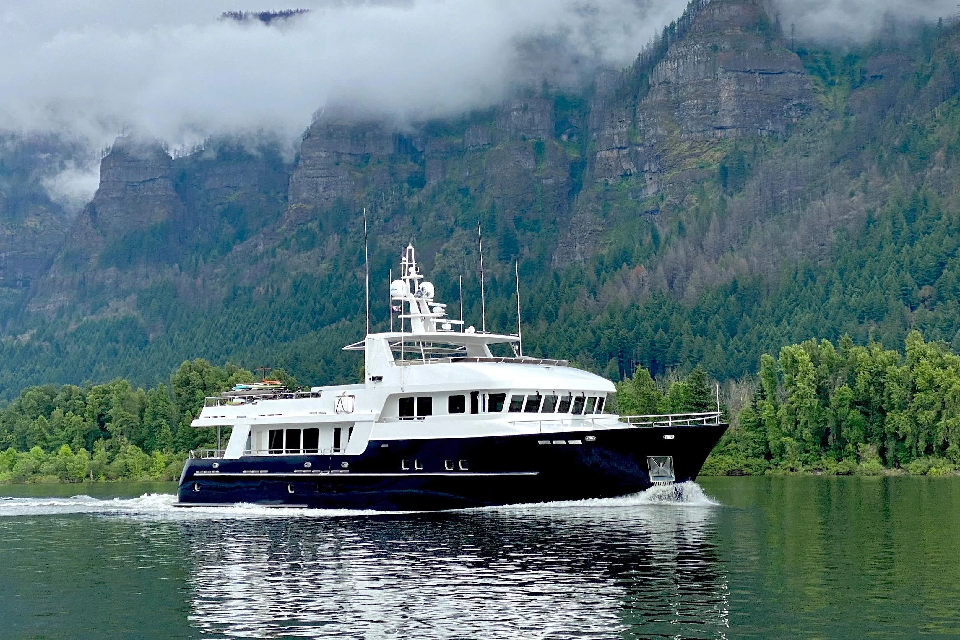 Luxurious 2017 Dauntless Custom yacht cruising on a serene lake with forested mountains.
