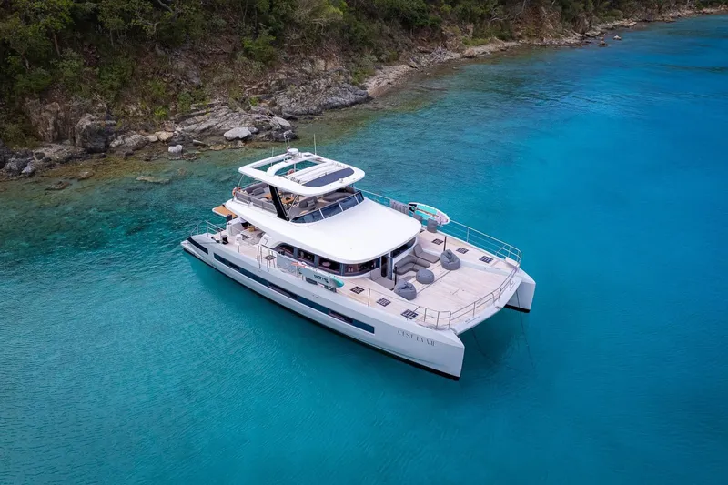 Cest La Vie Yacht Photos Pics Luxury Lagoon SIXTY 7 yacht, 2022 model, anchored in clear turquoise waters near a rocky shoreline.