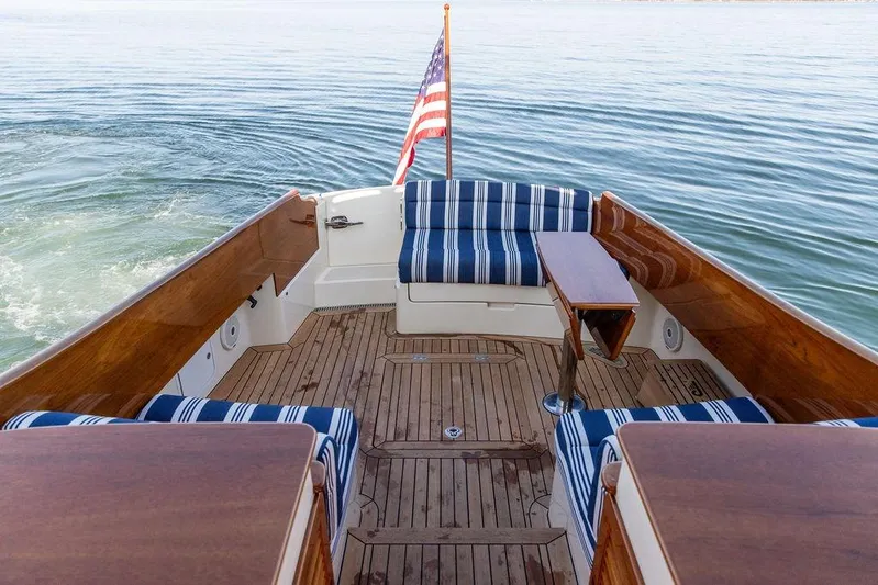 Pisces Yacht Photos Pics Hinckley Picnic Boat MKIII 2017 with striped seating, wooden deck, and American flag on calm water.