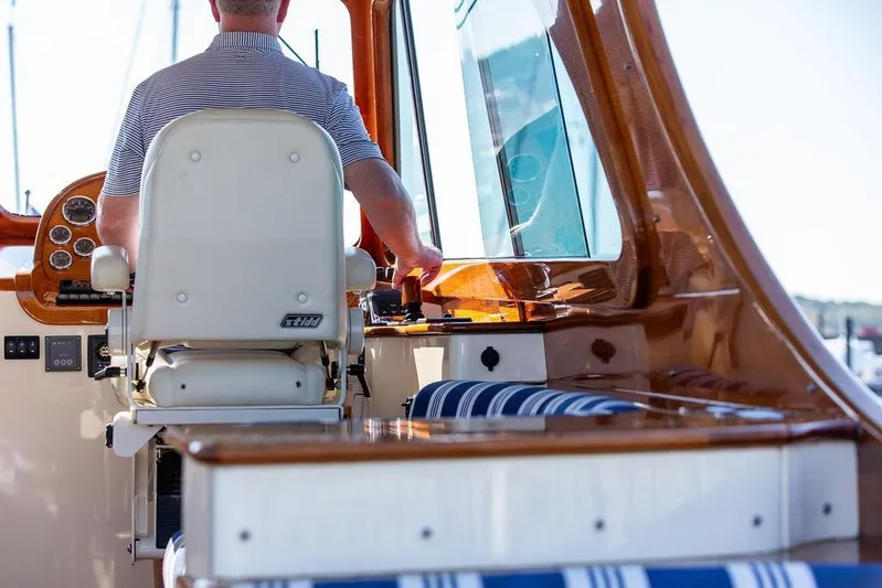 Pisces Yacht Photos Pics 2017 Hinckley Picnic Boat MKIII interior with captain at helm, featuring polished wood and striped seating.