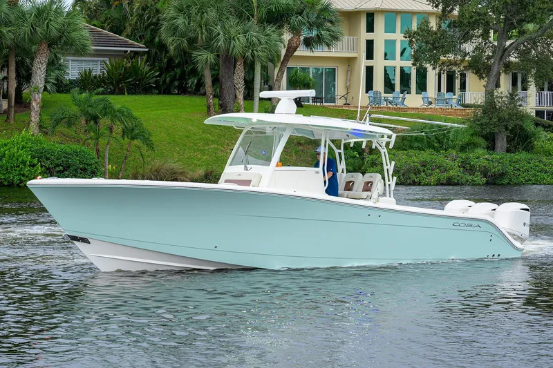 Conched Out Yacht Photos Pics 2020 Cobia 350 CC boat cruising on a scenic waterway near a luxurious waterfront home.