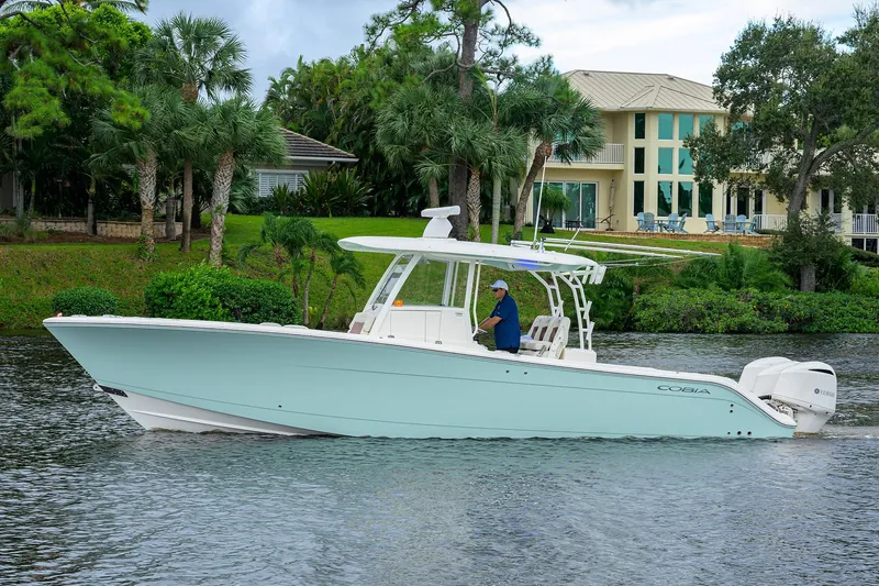 Conched Out Yacht Photos Pics 2020 Cobia 350 CC boat cruising on a scenic waterway near a luxurious waterfront home.