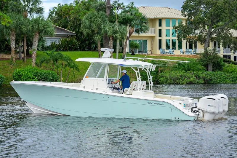 Conched Out Yacht Photos Pics 2020 Cobia 350 CC boat cruising on a scenic waterway near a luxurious waterfront home.