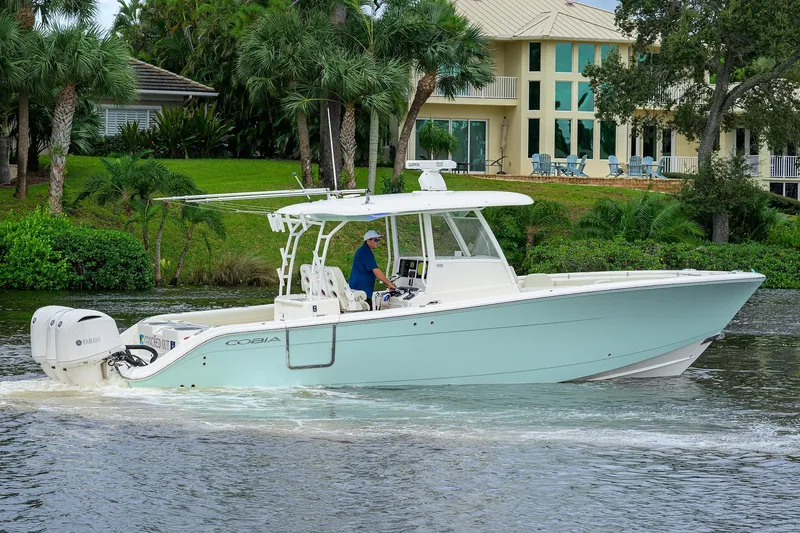 Conched Out Yacht Photos Pics 2020 Cobia 350 CC boat cruising on a scenic waterway near a luxurious house.