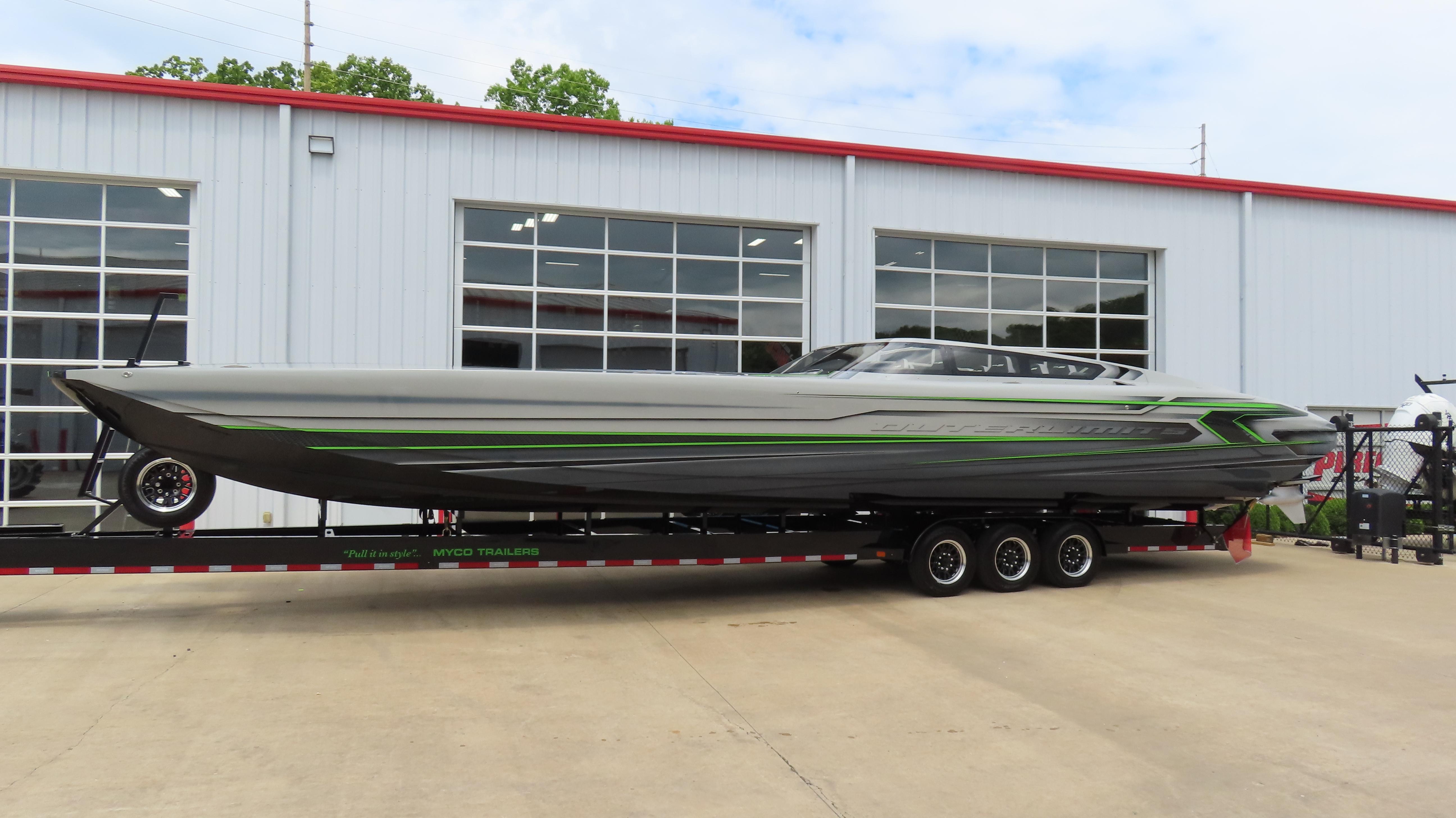 2025 Outerlimits 46 SC powerboat on trailer, sleek design with green accents, parked outside a building.