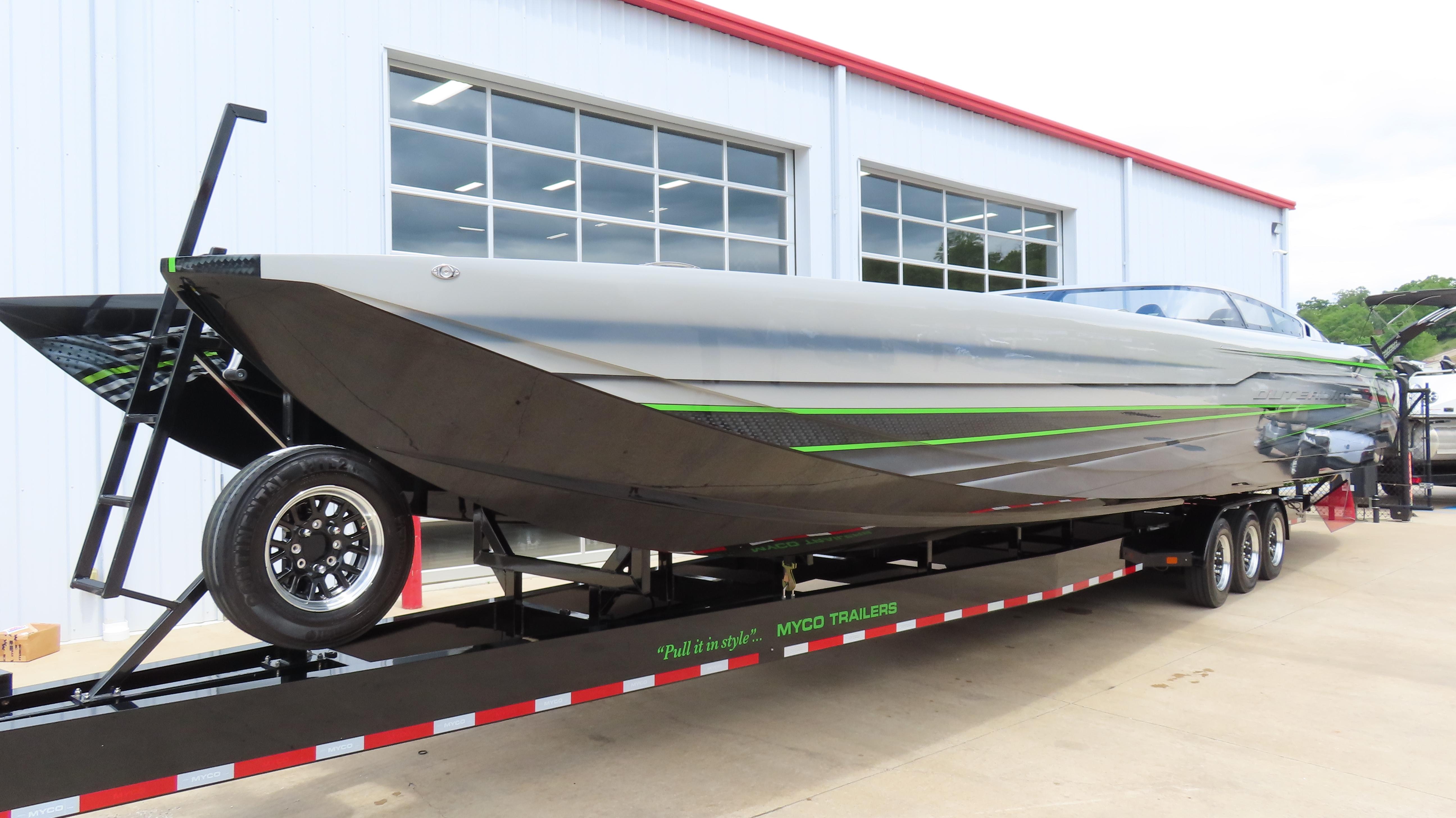 2025 Outerlimits 46 SC powerboat on trailer, sleek design with green accents, parked outside a building.
